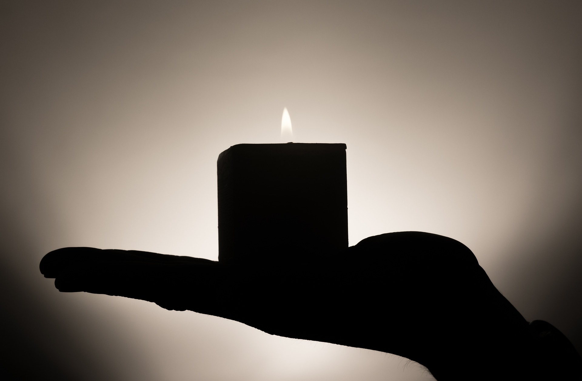Image of a shadowed hand holding a candle against a glowing wall.