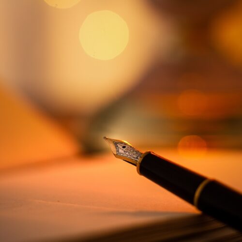A pen held above a notebook with an orange glowing background.