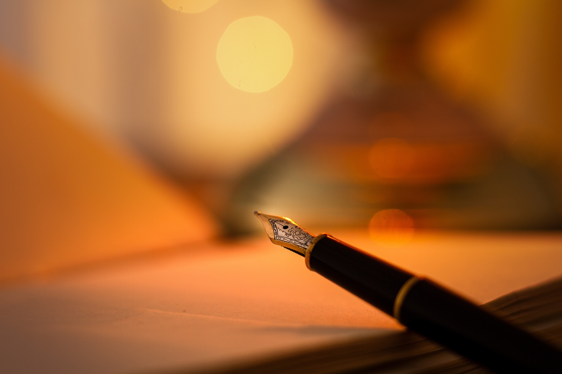 A pen held above a notebook with an orange glowing background.