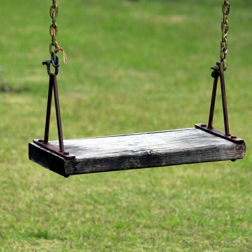 A wooden swing hanging in midair in front of green grass.