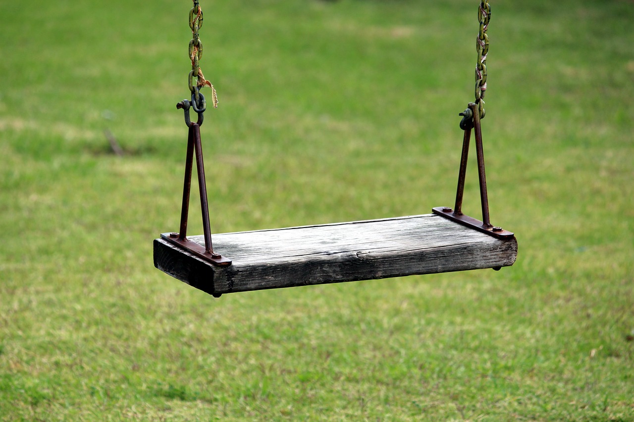A wooden swing hanging in midair in front of green grass.