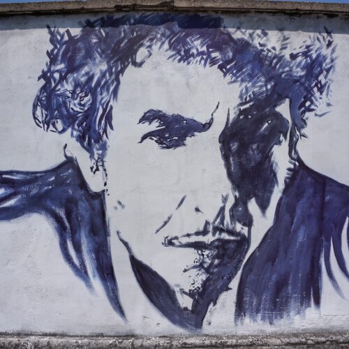 Image of a blue and grey mural of the musician Bob Dylan against a grey wall.