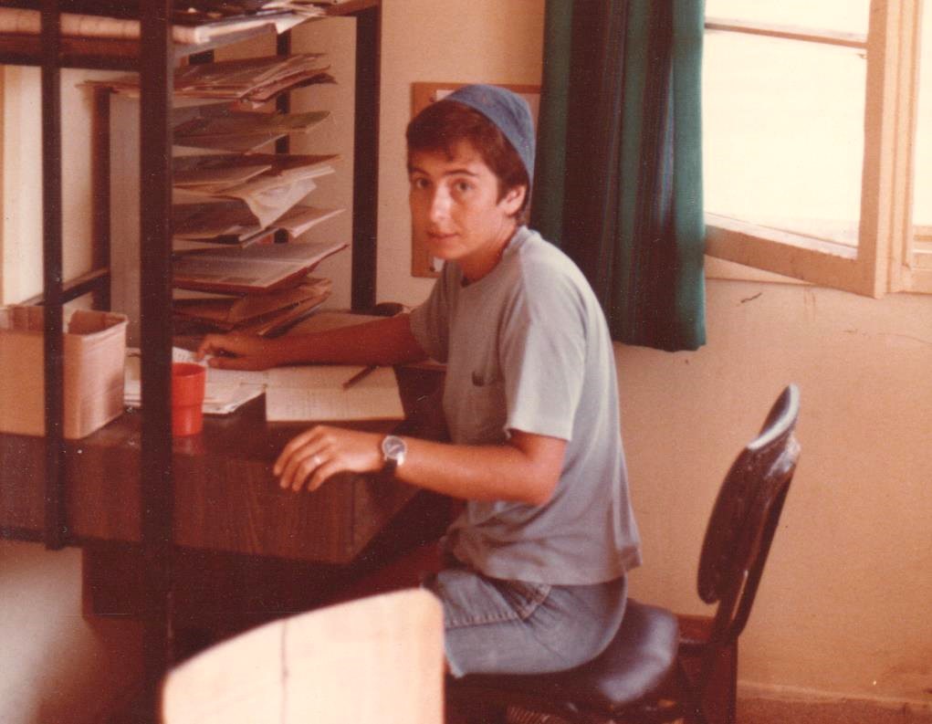 Vivian Silver, a young woman, wearing a grey shirt and jean shorts, sitting at a desk with shelves of papers and looking sideways into the camera. 