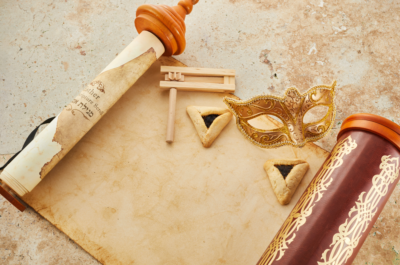 image of megillah scroll, with a wood grogger, 2 hamentaschen, and a gold mask upon it